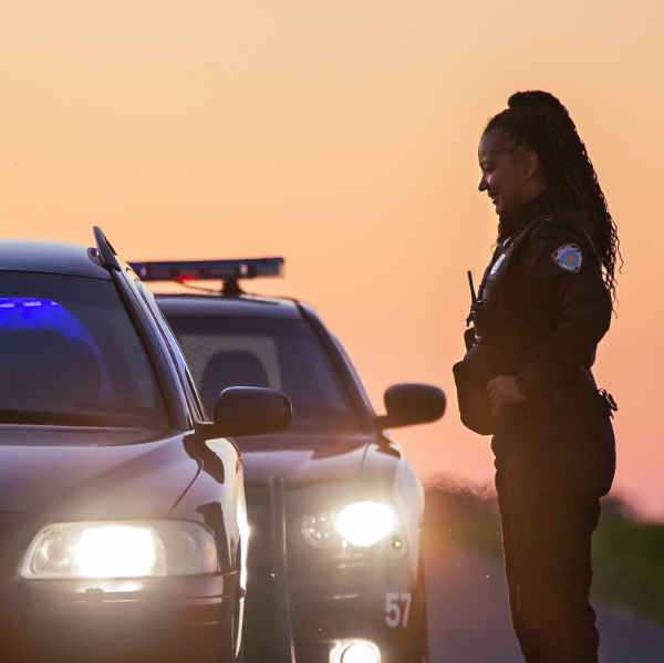 Police officer speaking to a driver as the driver is pulled over on the side of the road.